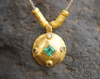 May include: A gold necklace with a round pendant featuring a green emerald gemstone surrounded by smaller diamonds. The pendant is textured and has a hammered finish.