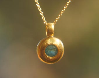 May include: A gold necklace with a round pendant featuring a blue gemstone.