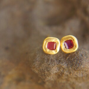 May include: A pair of gold earrings with small square red gemstones.