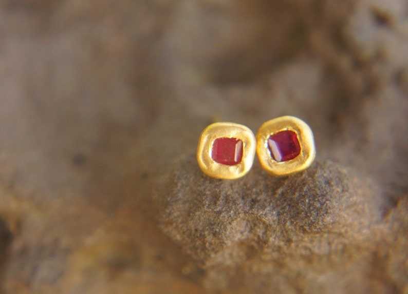 May include: A pair of gold earrings with small square red gemstones.