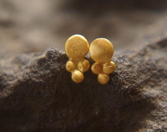 Puede incluir: Un par de pendientes de botón de oro con un diseño redondeado texturizado. Cada pendiente presenta un círculo más grande con tres círculos más pequeños agrupados debajo.