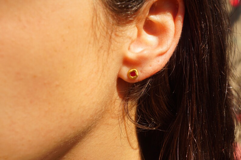 May include: A close-up of a person's ear with a small gold earring featuring a red gemstone.