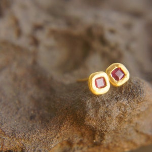 May include: A pair of gold earrings with small square red gemstones.
