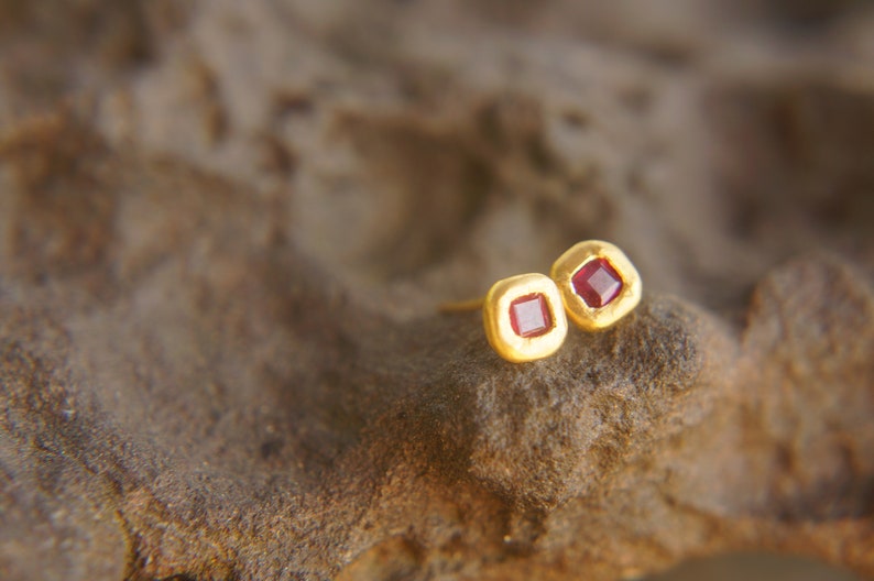 May include: A pair of gold earrings with small square red gemstones.