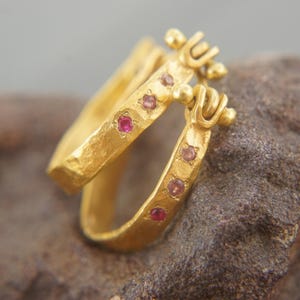 Puede incluir: Pendientes de aro de oro con acabado martillado y pequeñas piedras preciosas rosas. Los pendientes están diseñados para ser usados en pareja.