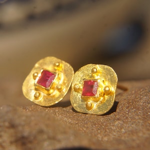 Puede incluir: Un par de pendientes de oro con piedras preciosas rojas cuadradas engastadas en un marco cuadrado.