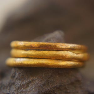 May include: Close-up of three gold-colored rings stacked on top of each other. The rings have a textured surface and appear to be made of metal. The rings are resting on a dark gray stone.