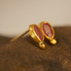 Puede incluir: Un par de pendientes de oro con peque&ntilde;as piedras preciosas rosas de forma ovalada. Los pendientes tienen un acabado texturizado y martillado.