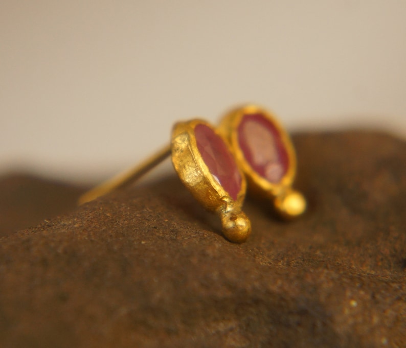 Puede incluir: Un par de pendientes de oro con peque&ntilde;as piedras preciosas rosas de forma ovalada. Los pendientes tienen un acabado texturizado y martillado.