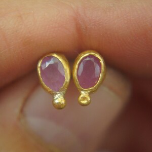 Puede incluir: Un par de pendientes de oro con piedras preciosas ovaladas de color rosa. Los pendientes tienen un dise&ntilde;o sencillo con una peque&ntilde;a bola de oro en la parte inferior de cada pendiente.