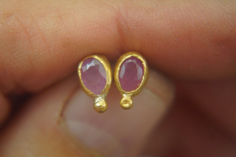Puede incluir: Un par de pendientes de oro con piedras preciosas ovaladas de color rosa. Los pendientes tienen un dise&ntilde;o sencillo con una peque&ntilde;a bola de oro en la parte inferior de cada pendiente.
