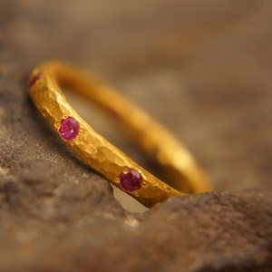 Może przedstawiać: Złoty pierścionek z fakturą młotkową i małymi czerwonymi kamieniami szlachetnymi osadzonymi w obrączce.