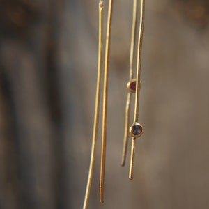 Könnte beinhalten: Ein Paar goldene Ohrringe mit kleinen violetten und roten Edelsteinen, die an dünnen goldenen Ketten hängen.