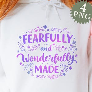 Puede incluir: Sudadera blanca con un diseño degradado en morado y rosa que dice "Fearfully and Wonderfully Made" rodeado de acentos florales.