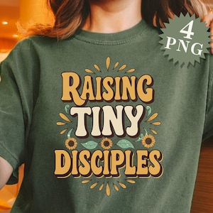 May include: A green t-shirt with the text "Raising Tiny Disciples" in a retro font. The text is surrounded by yellow sunflowers and green leaves.