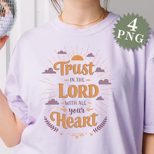 May include: A purple t-shirt with a graphic design that says "Trust in the Lord with all your heart". The graphic features a sun, clouds, and a floral design.