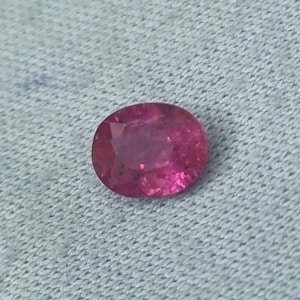Op de afbeelding: Een levendige roze ovaalvormige edelsteen met een glad, gepolijst oppervlak.