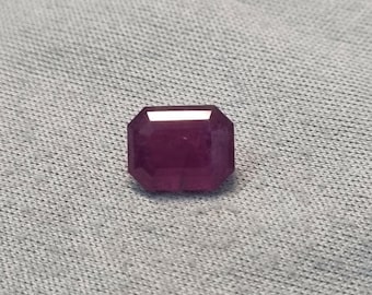 Puede incluir: Una piedra preciosa de color púrpura oscuro con un corte cuadrado esmeralda.