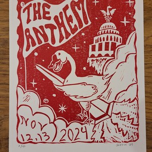 May include: Red and white linocut print titled "The Anthem." The artwork features a swan holding a flag with the title, the U.S. Capitol building, and the date November 12-13, 2024. Signed "SNIFFIN '24" and numbered 7/40.