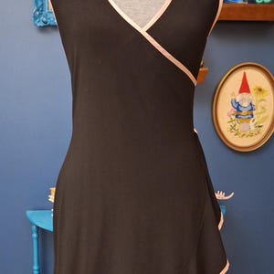 May include: A black sleeveless dress with a pink trim around the neckline and hem. The dress has a wrap style and a ruffled hem.