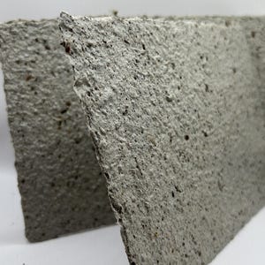 May include: Two gray, textured rectangular pieces of handmade paper, with rough edges and visible flecks. The paper has a slightly uneven surface, suggesting a natural, organic texture. The pieces are angled towards each other, creating a visual depth.