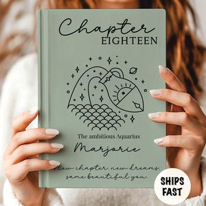 May include: A sage green hardcover book featuring the text Chapter EIGHTEEN, a black line art illustration of the Aquarius zodiac symbol, the text The ambitious Aquarius, the name Marjorie, and the phrase New chapter. new dreams. same beautiful you.