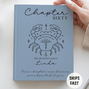 May include: A light blue journal with the text "Chapter Sixty" and a black crab illustration. Below the illustration, the text reads "The devoted Cancer Linda." The journal also includes the text "New chapter, new dreams, same beautiful you."