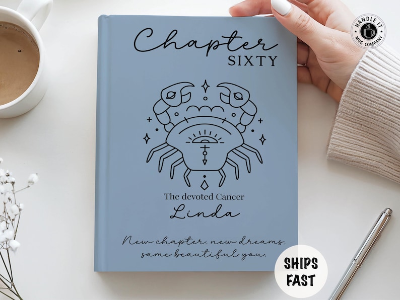 May include: A light blue journal with the text "Chapter Sixty" and a black crab illustration. Below the illustration, the text reads "The devoted Cancer Linda." The journal also includes the text "New chapter, new dreams, same beautiful you."
