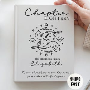 May include: A white hardcover book featuring the text Chapter Eighteen, a black line art illustration of two fish representing the Pisces zodiac sign, the name Elizabeth, and the phrase New chapter, new dreams, same beautiful you printed in black.