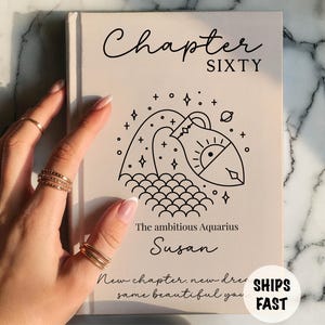 May include: A book cover with the words "Chapter SIXTY" in black script. Below is a black line drawing of an Aquarius symbol. The text "The ambitious Aquarius Susan" is below the drawing. The words "New chapter, new dress, same beautiful you" are at the bottom.