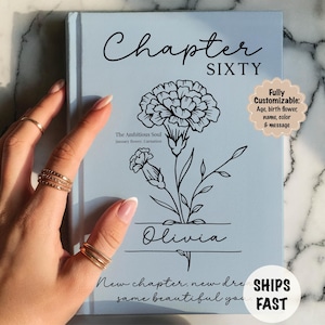May include: A light blue book cover with the words "Chapter Sixty" in black script. A black floral illustration and the name "Olivia" are featured. The text "New chapter, new dreams, same beautiful you" is at the bottom. The book is customizable.