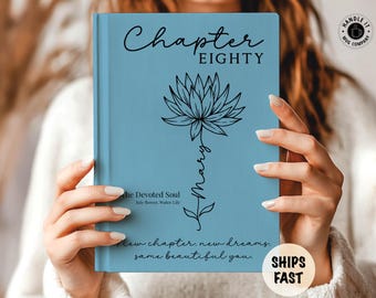 May include: A light blue hardcover journal featuring a black line art illustration of a water lily. The text reads Chapter EIGHTY, Mary, The Devoted Soul, July Flower, Water Lily, and New chapter. new dreams. same beautiful you. in black script and serif fonts.