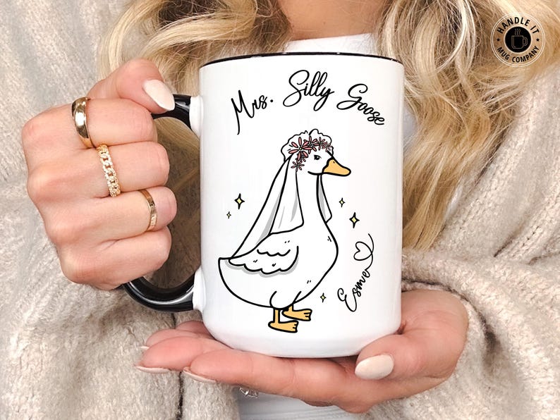 A blonde lady holding her Mrs Silly Goose mug gift that was gifted to her for her engagement party, wedding party or bridal shower. It appears to be the 15oz variant and allows for personalization.