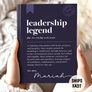 May include: A navy blue book with the words "leadership legend" in white. The book's definition is printed below the title. The name "Mariah" is written in cursive at the bottom. A circular sticker with the words "Number One" is in the upper right corner.