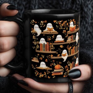 Gothic girl holding her Halloween mug gift with a repeating ghosts reading books pattern.