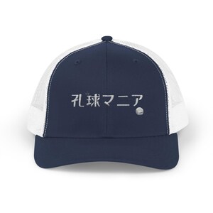 以下が含まれることがあります： 前面に日本語で「穴場」と刺繍されたネイビーブルーとホワイトのトラッカーハットです。