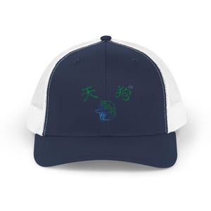 以下が含まれることがあります： 紺色と白のトラッカーハットに、緑と青の刺繍が施されています。デザインには「天狗」の文字と漫画のキャラクターが描かれています。