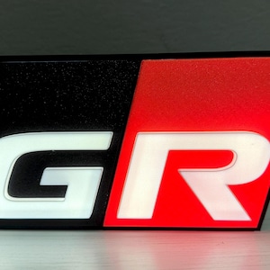 Könnte beinhalten: Ein schwarzes und rotes 3D-gedrucktes Emblem mit den Buchstaben "GR" in Weiß. Das "G" befindet sich auf einem schwarzen Hintergrund und das "R" auf einem roten Hintergrund.