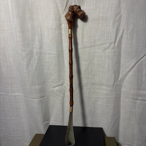 May include: A long shoehorn featuring a carved wooden handle shaped like a dog head. The handle connects to a bamboo-style wooden shaft with a brass-colored metal collar, ending in a smooth, curved, silver-toned metal scoop for the heel.