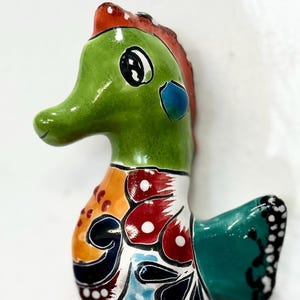 May include: A ceramic seahorse figurine with a glossy finish. The seahorse features a green head, orange tail, and a body adorned with colorful patterns including red, blue, and white floral designs. The seahorse is a decorative item.
