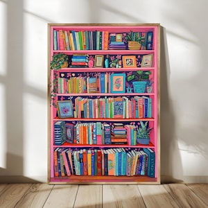 May include: A framed print of a bookshelf filled with colorful books, plants, and framed pictures. The bookshelf is painted pink with a dark blue floral wallpaper background. The books are various sizes and colors, creating a vibrant and inviting scene.