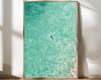 May include: An aerial view of a person swimming in a turquoise blue ocean. The water is clear and you can see the ripples and waves.