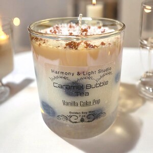 Könnte beinhalten: Eine durchsichtige Glas-Kerze mit einem braunen und weißen, geschichteten Wachsdesign. Die Kerze ist mit "Harmony & Light Studio Caramel Bubble Tea Vanilla Cake Pop Golden Soy Wax 7 oz." beschriftet.