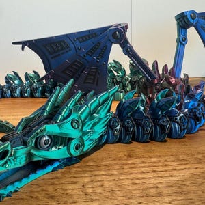 May include: A multi-colored, articulated dragon model with a metallic finish. The dragon is made of plastic and has a segmented body, wings, and head. The dragon is posed in a flying position with its wings spread out.
