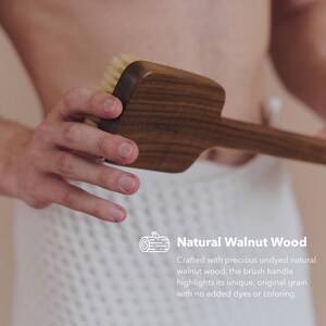 May include: A wooden body brush made of natural walnut wood. The brush has a long handle and a rectangular head with soft bristles. The text "Natural Walnut Wood" is visible.