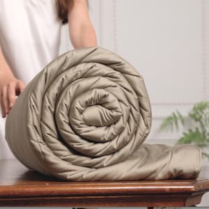 May include: A rolled up beige weighted blanket with a quilted design. The blanket is on a wooden table.