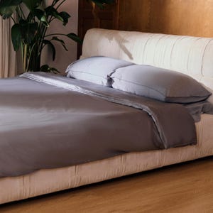 May include: A gray duvet cover on a white upholstered bed with two white pillows. The bed is in a bedroom with a wooden floor.