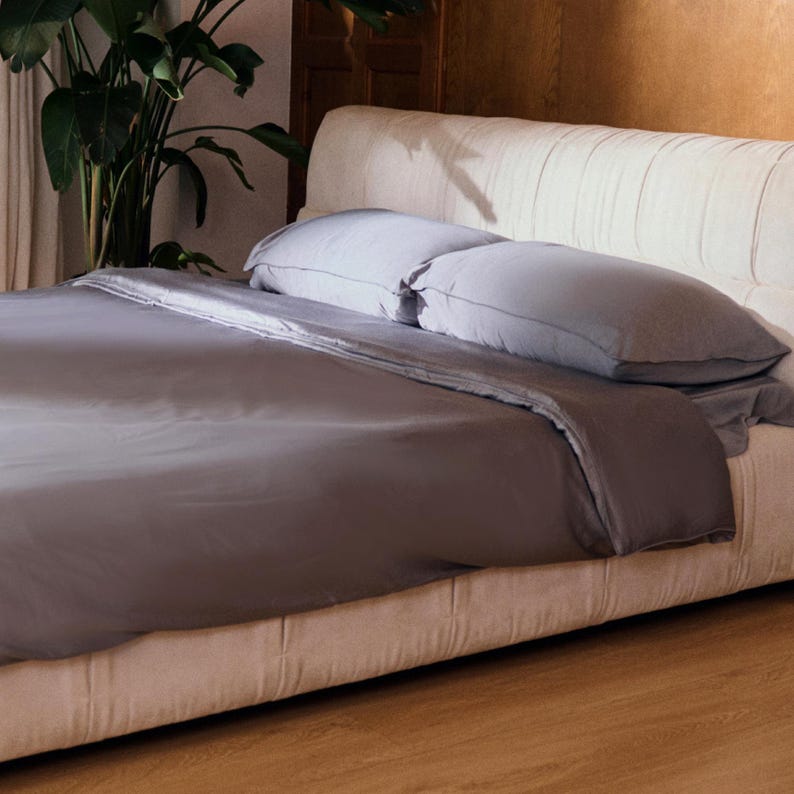 May include: A gray duvet cover on a white upholstered bed with two white pillows. The bed is in a bedroom with a wooden floor.