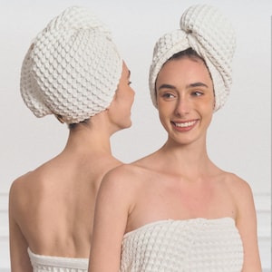 Puede incluir: Dos mujeres con toallas para el cabello blancas con tejido de gofre y toallas envolventes a juego. Las toallas están envueltas alrededor de sus cabezas y cuerpos. El fondo es blanco liso.
