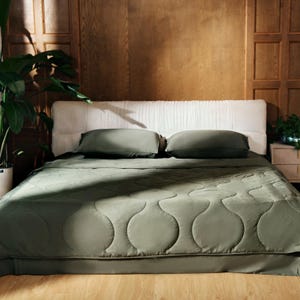 May include: A green quilted bedspread with a white headboard and two green pillows. The bed is in a room with wood paneling on the walls.